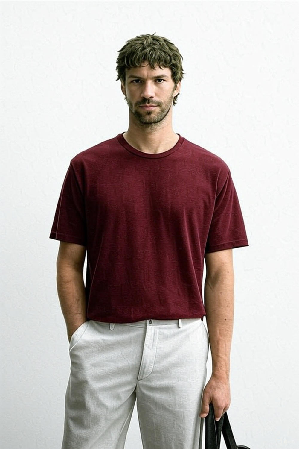 Man wearing a maroon t-shirt and light-colored pants against a white background