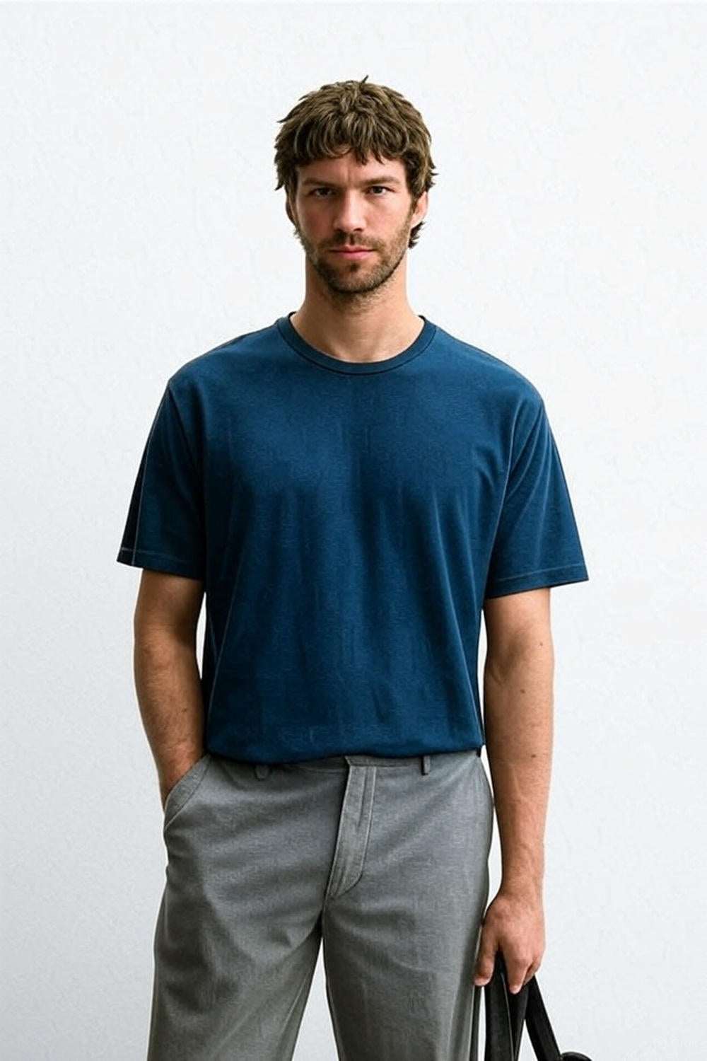 Man wearing a blue t-shirt and gray pants against a white background