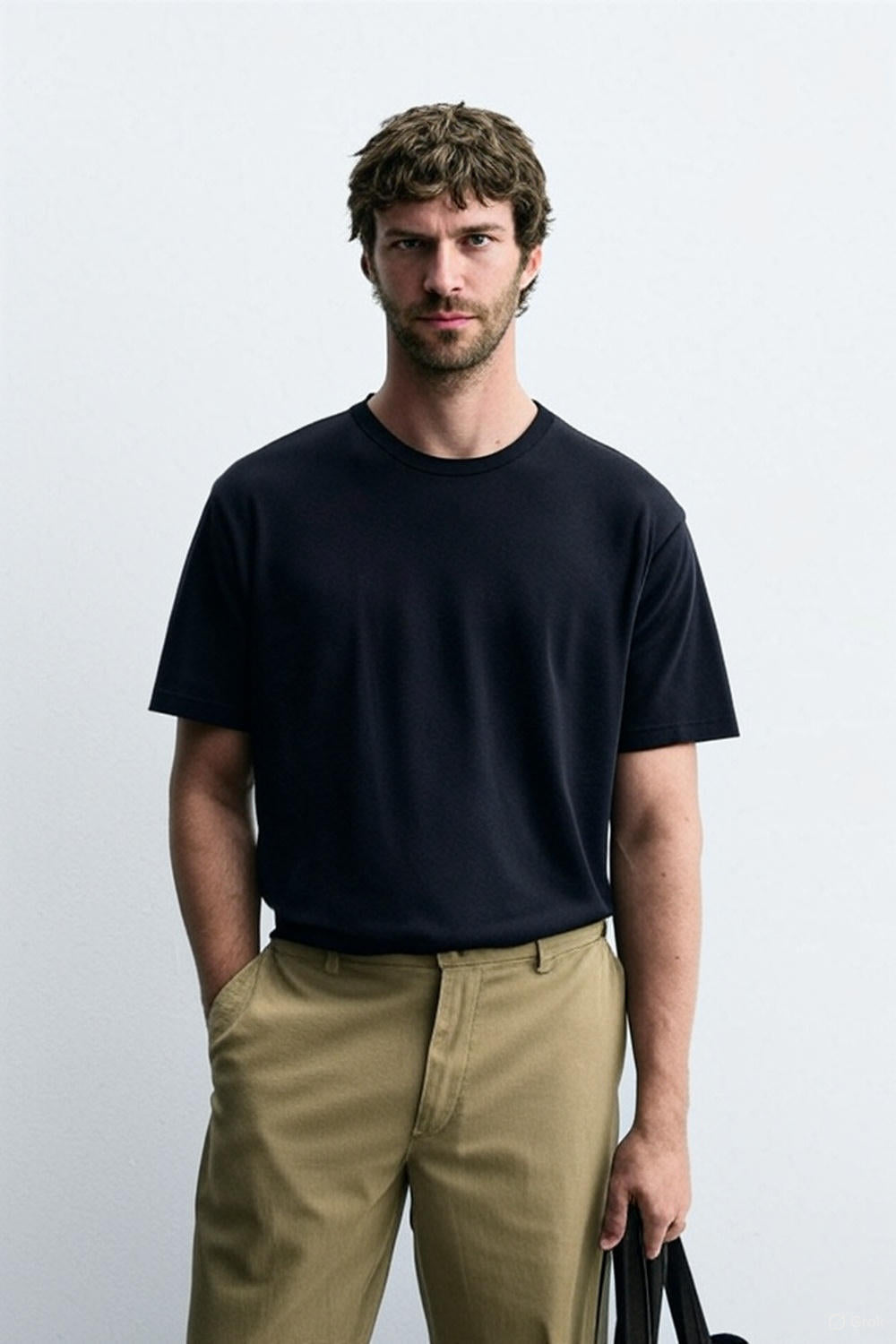 Man wearing a black t-shirt and beige pants against a white background