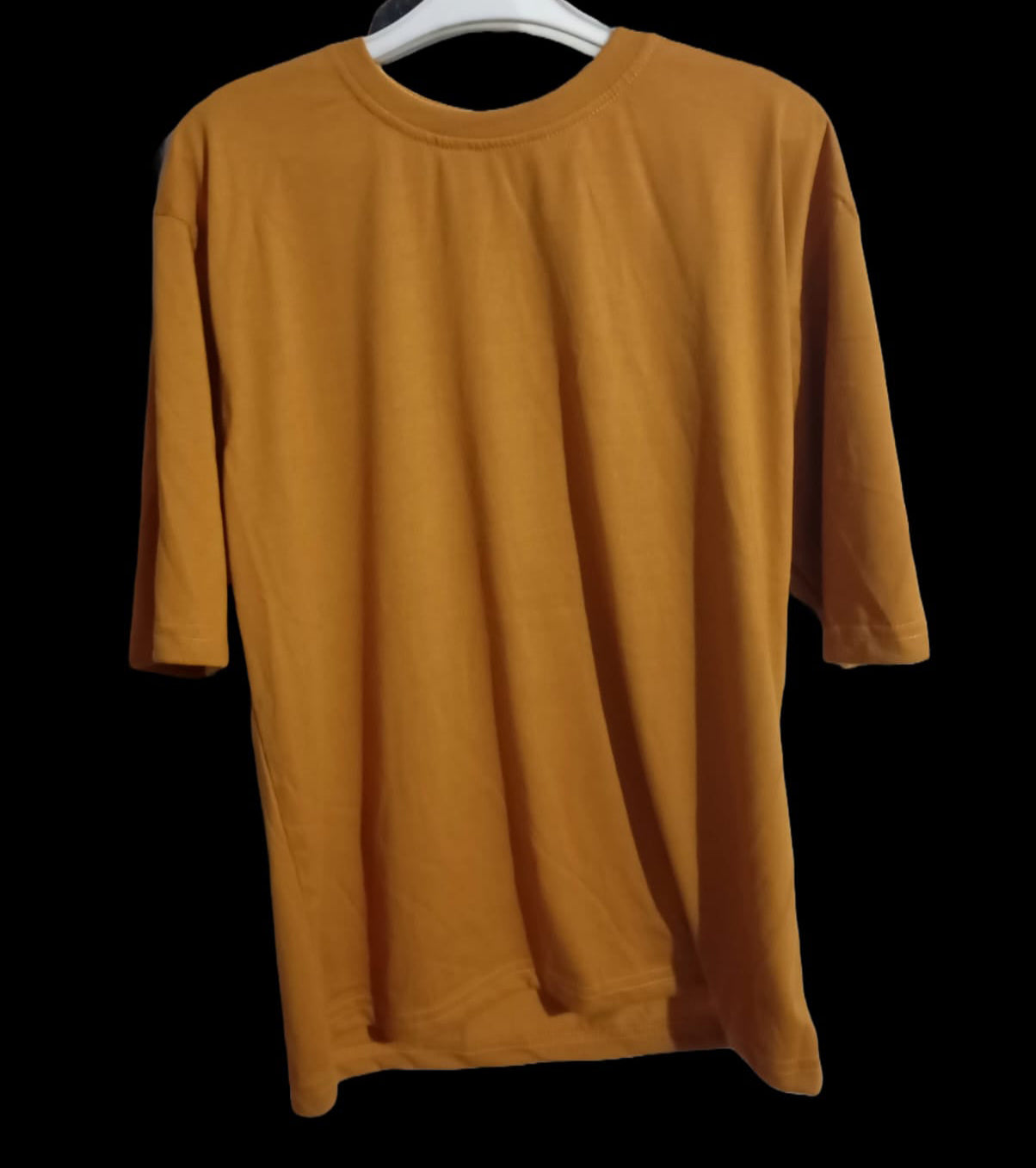 Mustard yellow long-sleeve shirt on a white hanger against a black background